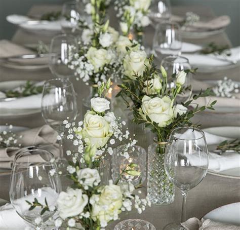 The Table Is Set With White Flowers And Silverware