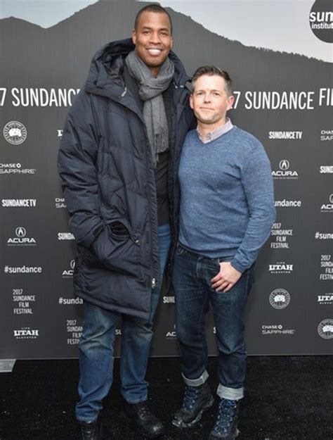 Two Men Standing Next To Each Other On A Black Carpet