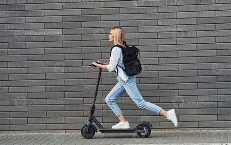 Side View Of Beautiful Blonde In Casual Clothes That Riding Electric Schooter Outdoors At Sunny