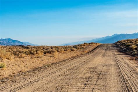 Dirt Road In Desert Valley Heading Toward Distant Mountains Stock Photo