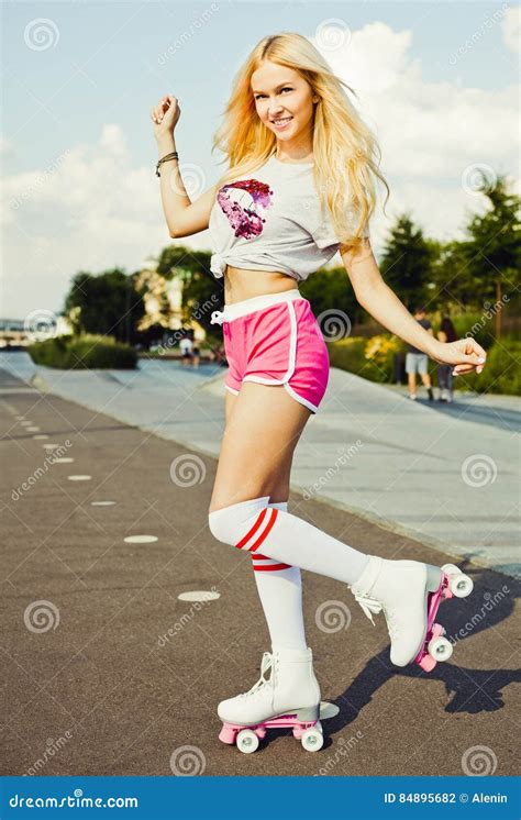 beautiful blonde girl posing on a vintage roller skates in pink shorts and white t shirt in the