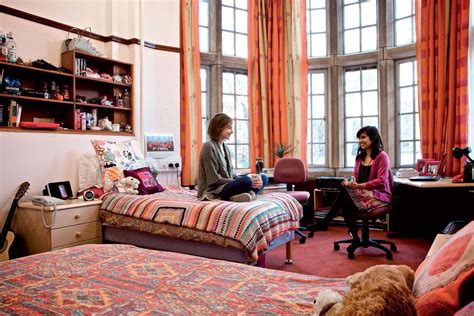 Two Women Sitting On The Bed In A Room With Large Windows And Colorful