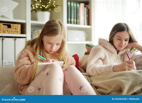 Two Cute Young Sisters Studying Or Sketching Snuggled Up On The Sofa In