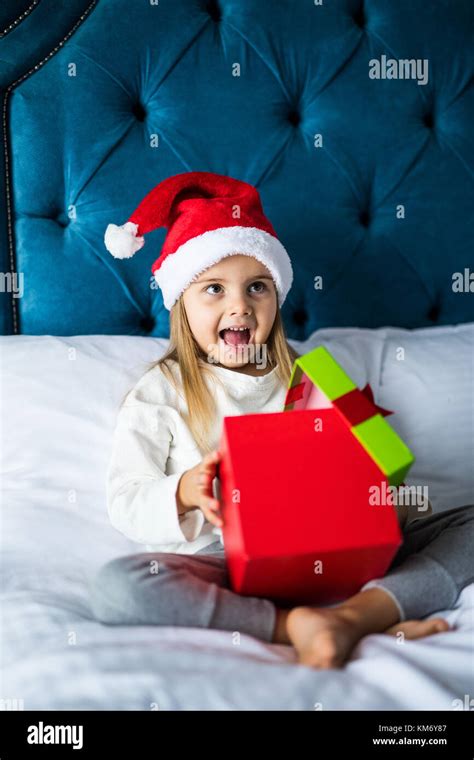 Surprised Little Girl In Santas Hat Holding Present While Sitting With