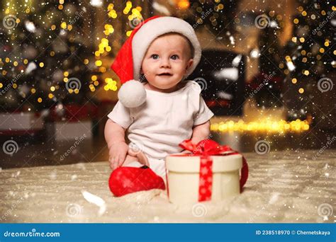 Cute Baby In Santa Hat With Christmas T On Floor At Home Stock Photo