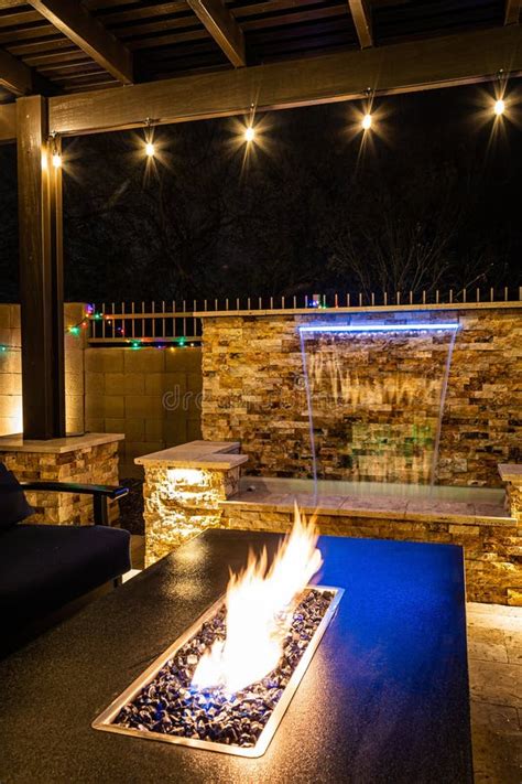 A Resort Style Backyard At Night With A Waterfall Pergola And A