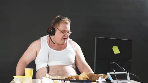 hombre gordo con gafas y auriculares sentado en una mesa comiendo y jugando un juego de pc en