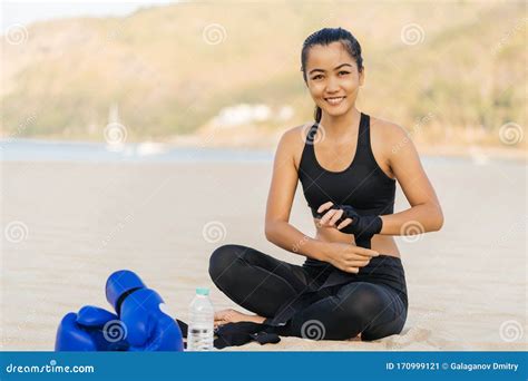 Asian Athletic Woman In Sportswear Sitting On The Beach And Holding