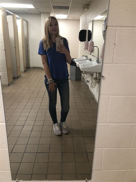 A Woman Taking A Selfie In A Public Restroom With A Mirror On The Wall