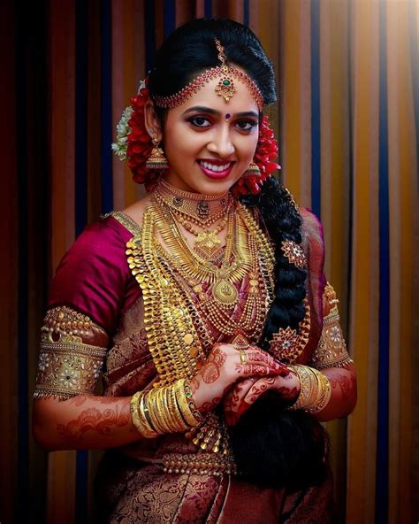 A Woman In A Red And Gold Sari With Her Hands On Her Chest Smiling