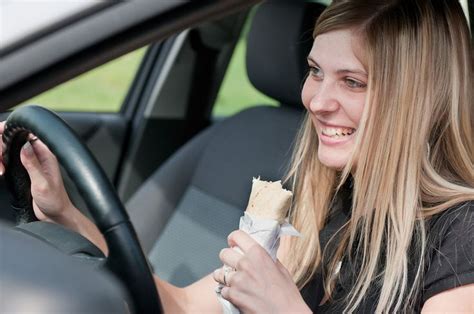 a woman sitting in the driver seat of a car eating something out of her hand