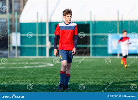 Boys In Red And Blue Sportswear Plays Football On Field Dribbles Ball