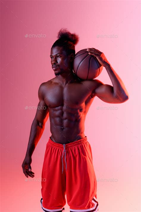 Confident Shirtless African American Sportsman Looking Away While Holding Ball On Pink