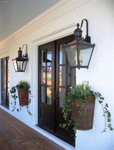 Two Potted Plants Sit On The Front Porch Of A White House With Black Doors