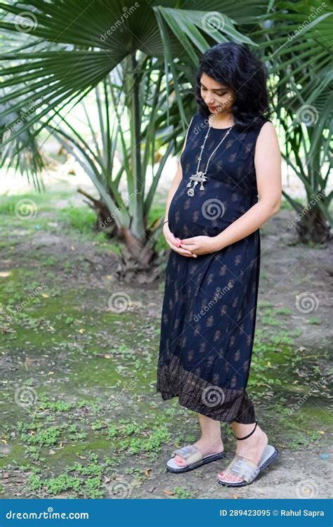 a pregnant indian lady poses for outdoor pregnancy shoot and hands on belly indian pregnant