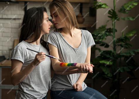 mujer joven lesbiana pintando la bandera del arco iris sobre la mano de su novia foto gratis