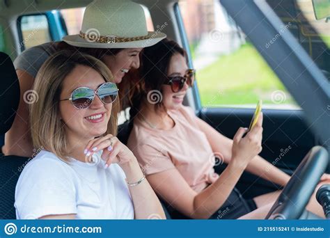 Three Happy Girlfriends Go On A Trip Women Ride In The Car Look At The Phone And Laugh Stock