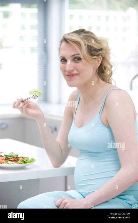 pregnant female fair hair tied at the back wearing a blue vest and blue trousers sitting in