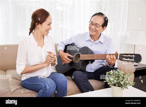 Happy Admiring Senior Woman Clapping To Her Husband Playing Acoustic Guitar And Singing Song