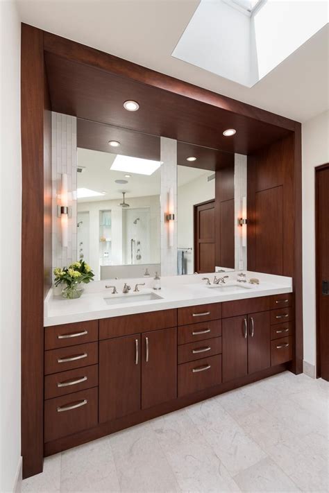 Contemporary bathroom features a frameless vanity mirror fitted with custom behind mirror lighting that's illuminating white and silver hex backsplash tiles and a white quartz countertops holding an undermount sink and polished nickel modern faucet positioned over flat front lacquered gray vanity. A built-in double vanity features sleek woods, chic white ...