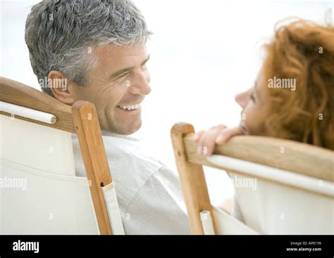 Mature Couple Sitting In Deck Chairs Smiling At Each Other Stock