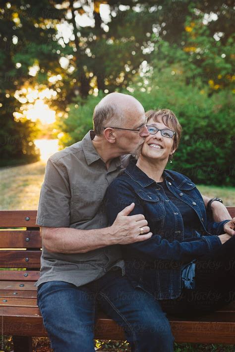 Middle Aged Retired Couple Kissing And Cuddling Outside Sitting On A