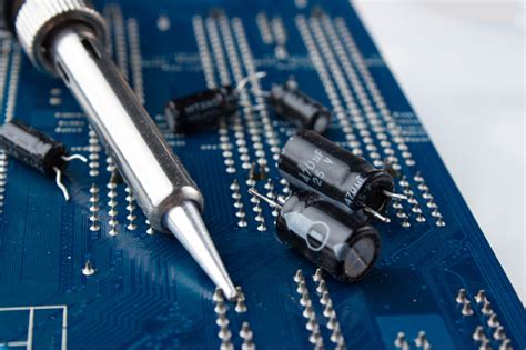 Soldering Iron On The Background Of A Computer Board And Capacitors In