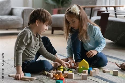 Concentrated Little Brother And Sister Sit On Warm Floor In Living Room