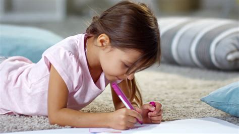 Medium Shot Of Cute Little Schoolgirl Lying On The Floor And Drawing