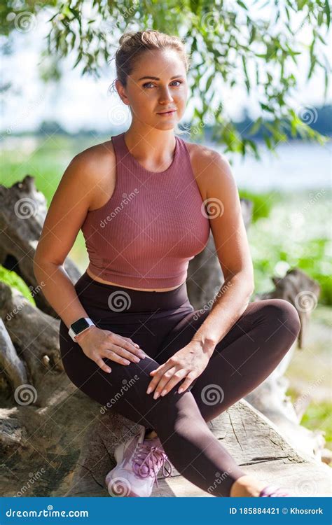 attractive woman in yoga pants and top sitting in forest taking rest after trainings looking at