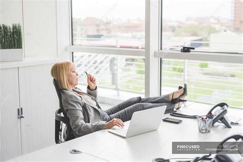 Mature Businesswoman With Feet Up On Office Desk — Female