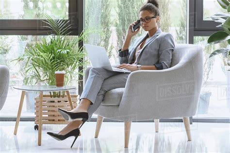 African American Businesswoman Sitting In Armchair And Talking On Smartphone While Working On