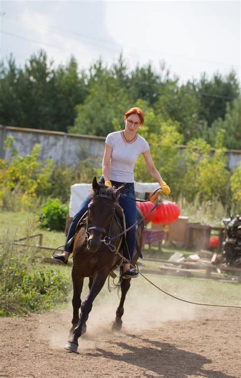 A Redhead Woman Riding A Horse On The Field A Green Bush On A