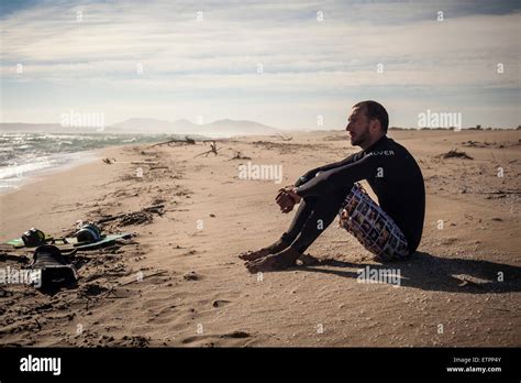 Kite Surfer In Wet Suit Sitting On Beach Thoughtful Wistful Beach