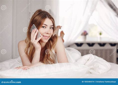 Cute Smiling Girl Looks At The Phone Lying On The Bed A Girl Reads