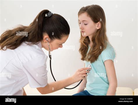 Young Female Doctor Examining Girl With Stethoscope In Hospital Stock