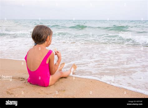 The Girl In The Pink Bathing Suit Sitting On The Beach Eating A Stock Photo Alamy
