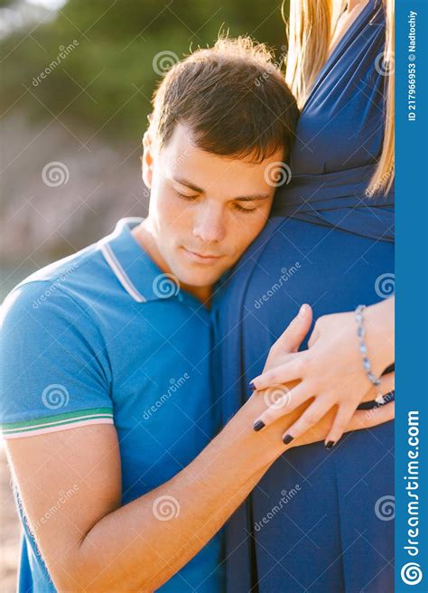 Man Put His Ear To The Belly Of Pregnant Woman In A Long Blue Dress On A Sunny Day Stock Image