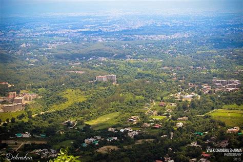 An Aerial View Of A City Surrounded By Lush Green Hills And Trees In
