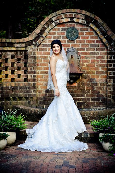 A Woman Standing In Front Of A Brick Wall Wearing A White Wedding Dress