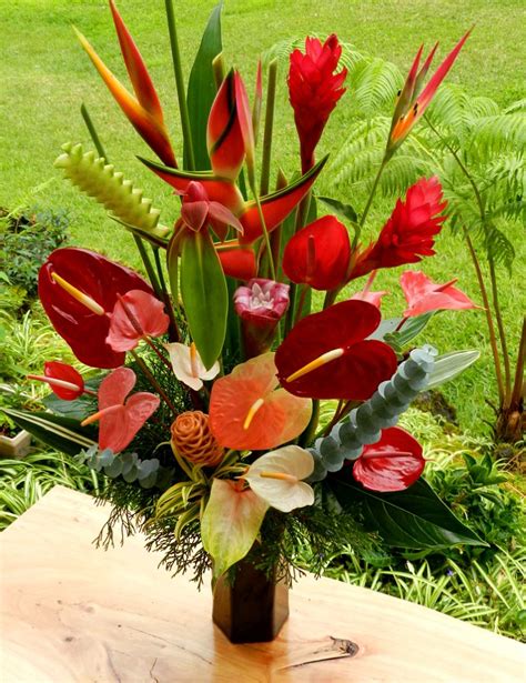 A Vase Filled With Red And Orange Flowers On Top Of A Wooden Table Next To Grass