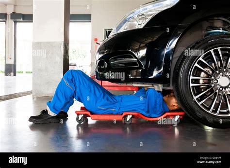 Mechanic In Blue Uniform Lying Down And Working Under Car At Auto