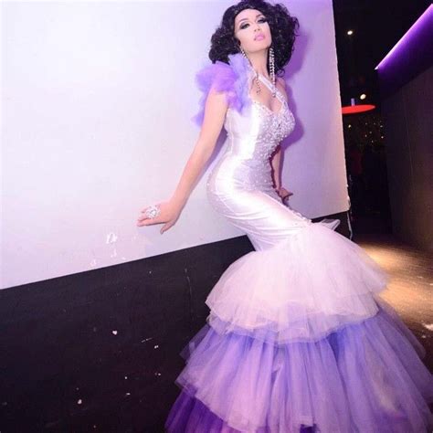 A Woman In A Purple And White Dress Standing Next To A Wall With Lights