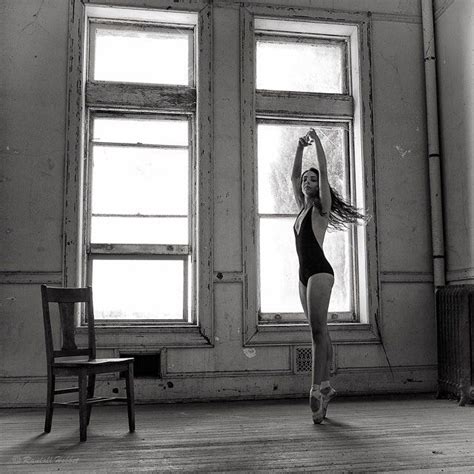 A Woman In A Black Leotard Is Standing By A Window And Stretching Her Arms