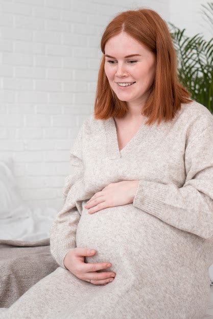 premium photo redhead pregnant woman in warm cozy dress puts hands on stomach sitting in