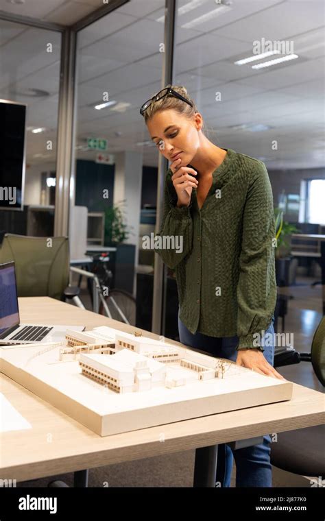 Thoughtful Caucasian Female Architect Examining Architectural Model On