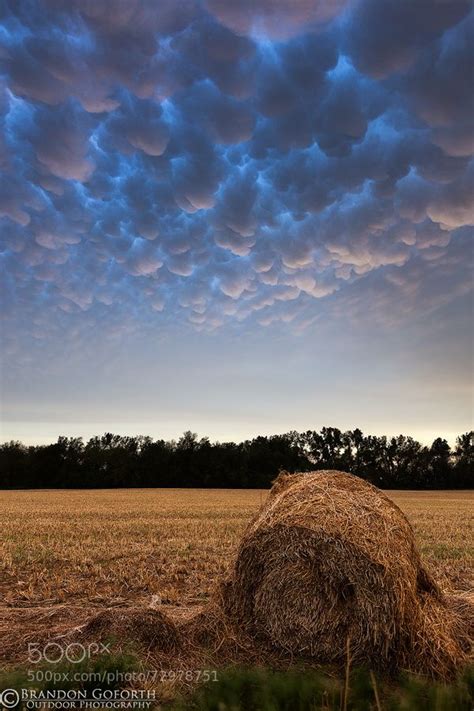 A Bale Of Hay Sitting In The Middle Of A Field Under A Cloudy Sky