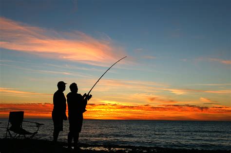 A Silhouette Of Two Men Fishing At Sunset Stock Photo Download Image