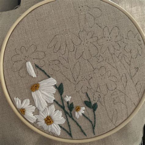A Close Up Of A Embroidery On A Pillow With White Daisies In The Center