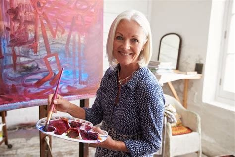 Portrait Of Female Artist Working On Painting In Studio Stock Photo